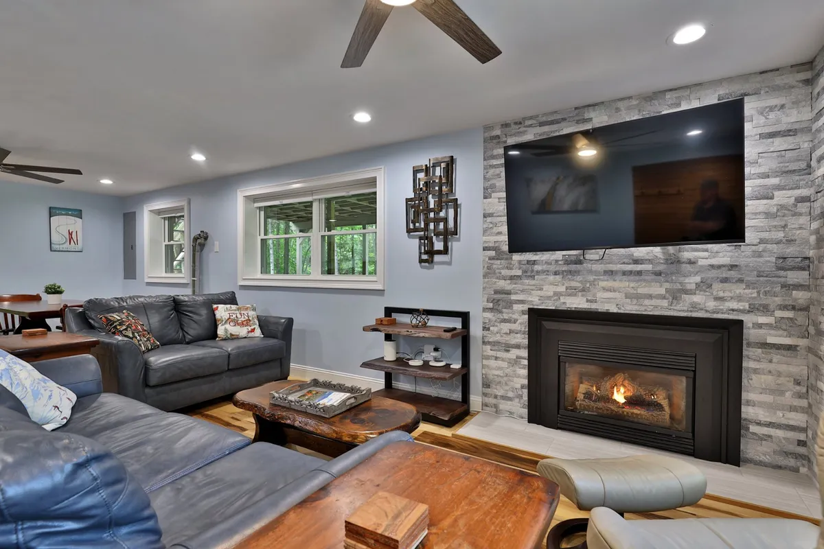 A comfortable seating area with a sofa facing a fireplace and a mounted television, complemented by a wooden table. The atmosphere is homely and encourages gathering, relaxation, and storytelling after a day of adventure.