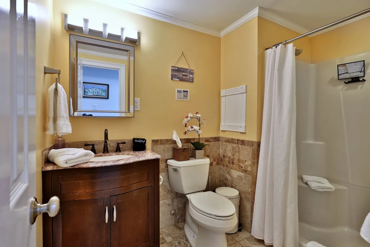 A modern bathroom with a wooden vanity, round mirror, tiled backsplash, and a visible shower area. The mood is calming and refreshing, ideal for unwinding and daily routines.