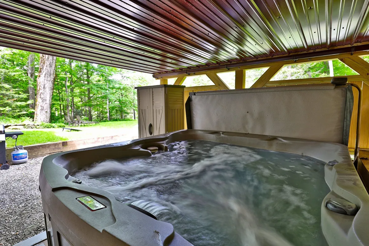 This interior image features a private hot tub nestled within a wooden structure, with lush greenery visible just outside. The setting is serene and evokes relaxation, emphasizing a strong connection to nature while providing privacy. The inviting ambiance suggests both peaceful solo soaks and social moments.