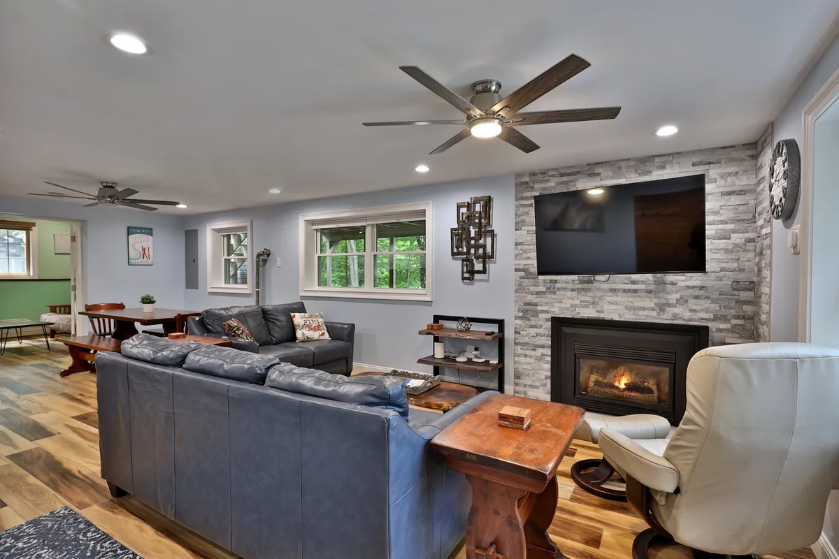A welcoming living room featuring a plush sofa set around a flickering gas fireplace, a wooden coffee table at the center, and a wall-mounted smart TV. The setting is enhanced by warm lighting and inviting decor, making it perfect for group relaxation and entertainment.