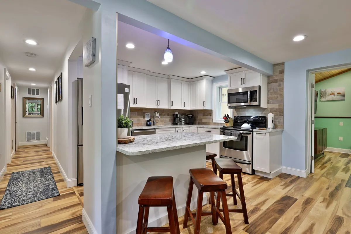 A bright, inviting kitchen with a prominent island, bar stools, white cabinetry, and stainless steel appliances. The kitchen island offers ample space for casual breakfasts or snacks, and the overall layout emphasizes openness and connectivity to surrounding areas.