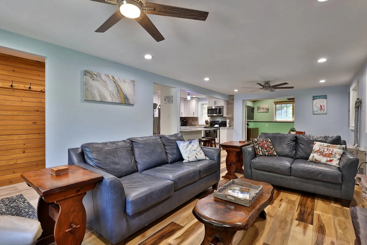 A cozy interior living space with leather sofas, a wooden coffee table, and an open view to the kitchen area. Decorative pillows and a warm ambiance suggest a space ideal for family gatherings, celebrating, or relaxing together after a day of exploration.