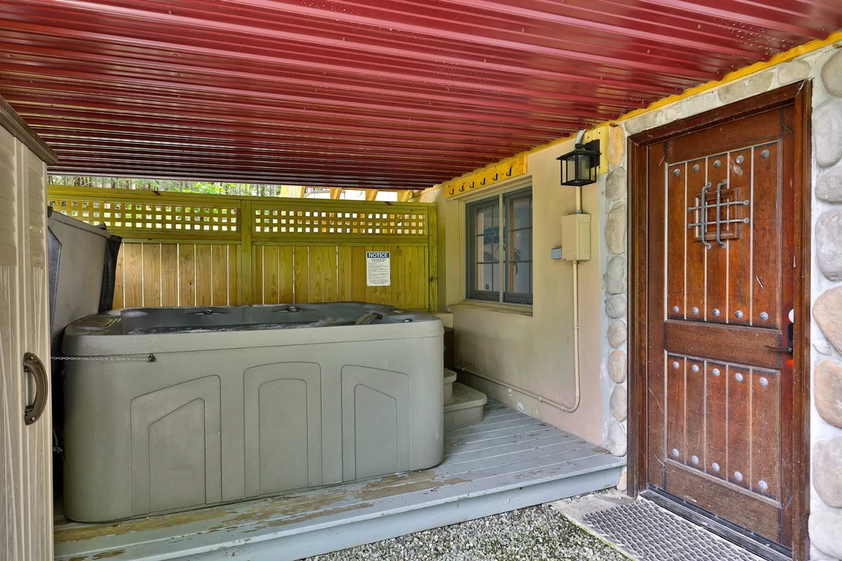An exterior shot captures the hot tub set beside a rustic wooden door and a stone wall, blending nature with architectural charm. This space is equally inviting during the day or night, suggesting relaxation under the stars or group gatherings on chilly evenings.