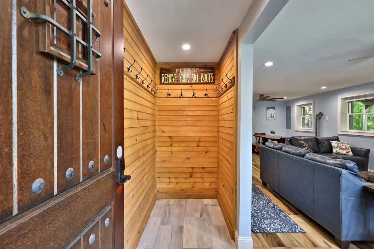 A functional and inviting mudroom with a wooden door, wood paneling, and hooks for ski gear. The space is organized for storing and drying outdoor equipment, ideal for managing gear after a day outside.