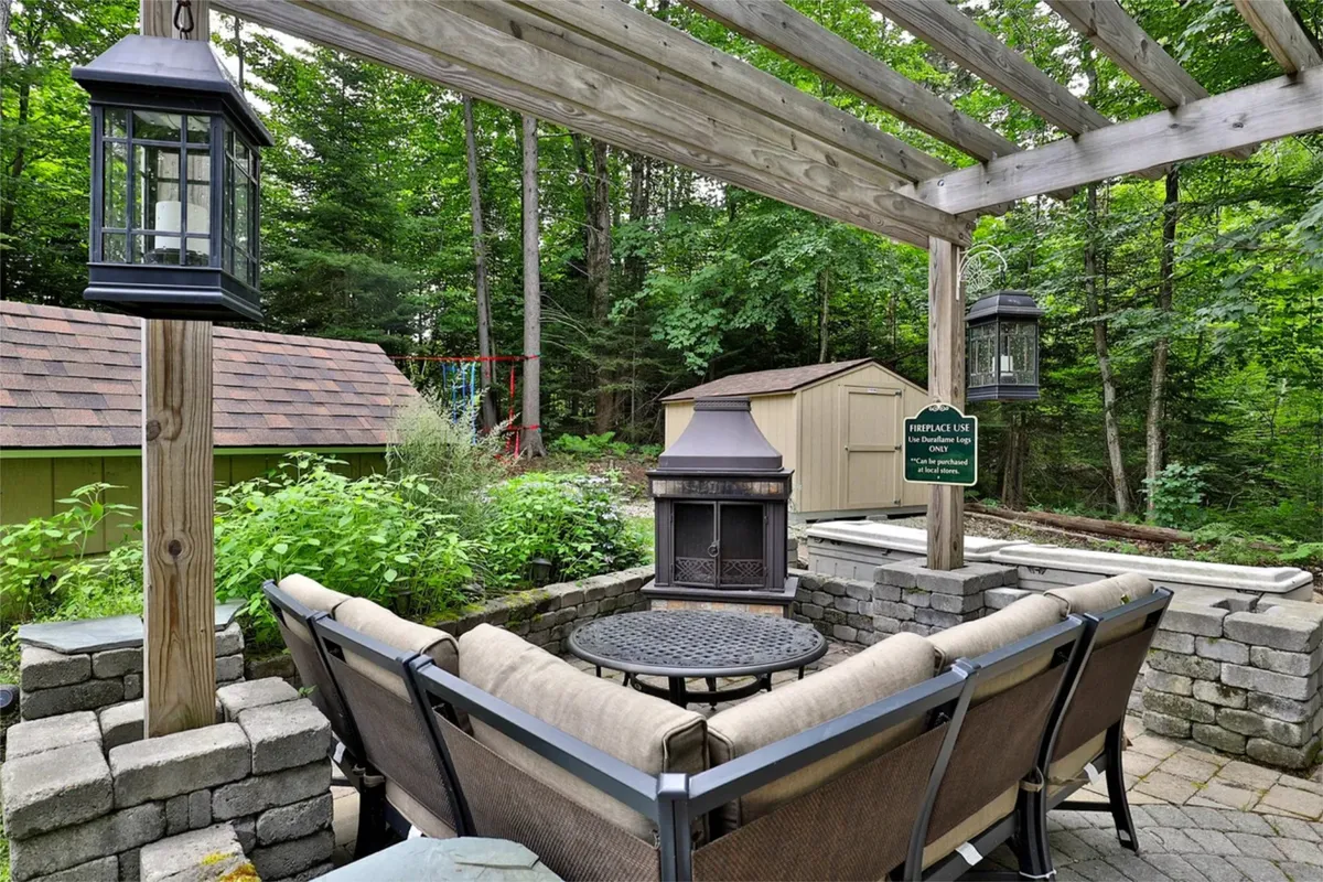 This exterior image displays a cozy fire pit seating area beneath a pergola, surrounded by lush greenery. The setting invites guests to gather for fireside chats, stargazing, or relaxed evenings outdoors, capturing the shared aspect of the property's amenities.