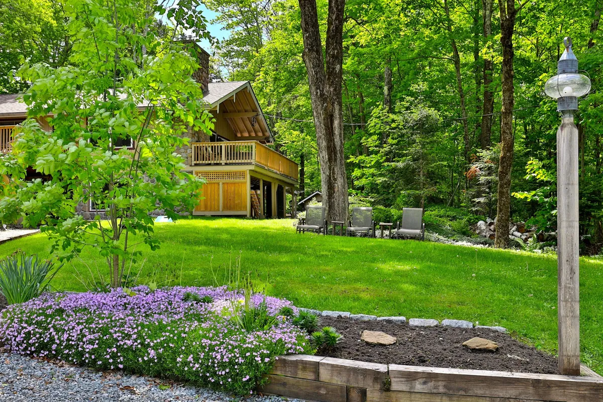 This image shows a serene wooden deck surrounded by vibrant flower beds and a well-maintained lawn. A comfortable seating arrangement invites guests to relax and enjoy the tranquility of the outdoors. The setting is lush, private, and nestled in nature, reflecting a peaceful Vermont retreat.